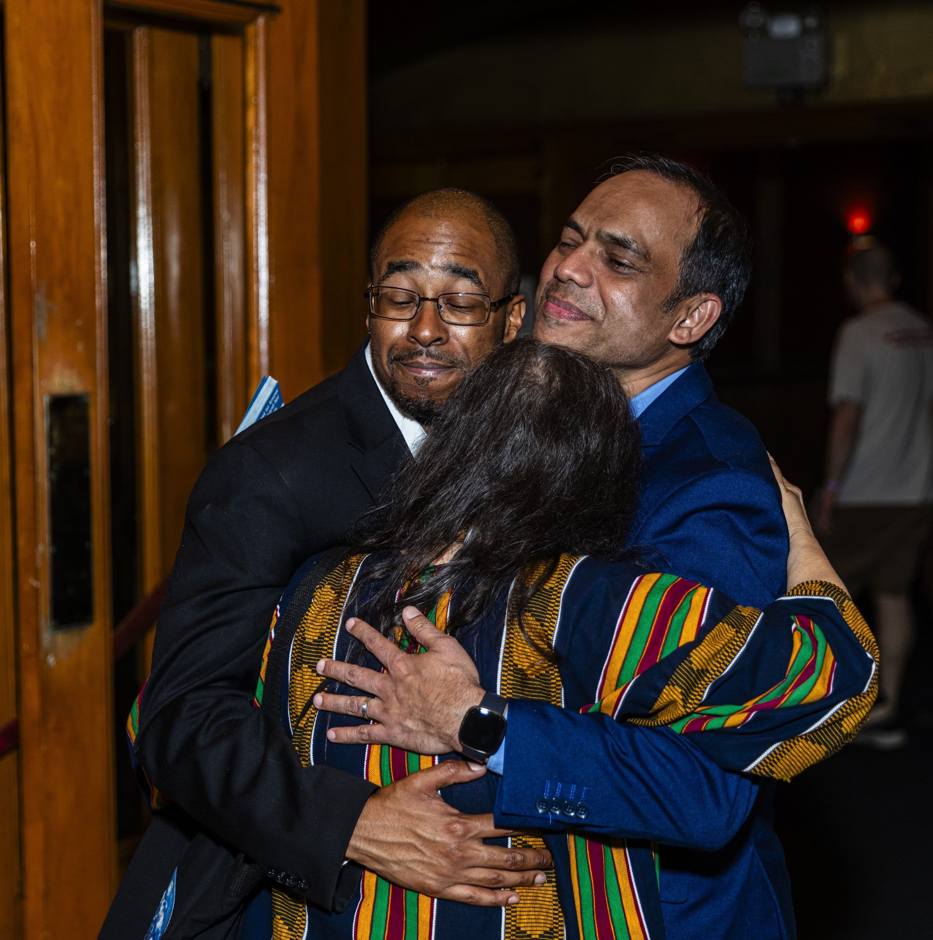 Rais Bhuiyan and two other people in a three-way embrace in a theatre foyer after a screening.